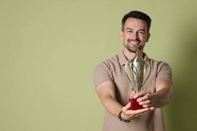 Photo of Happy winner with golden trophy cup on pale olive background, space for text