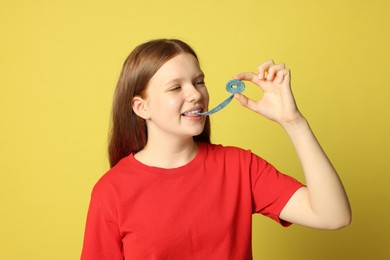 Photo of Teenage girl eating tasty gummy candy on yellow background