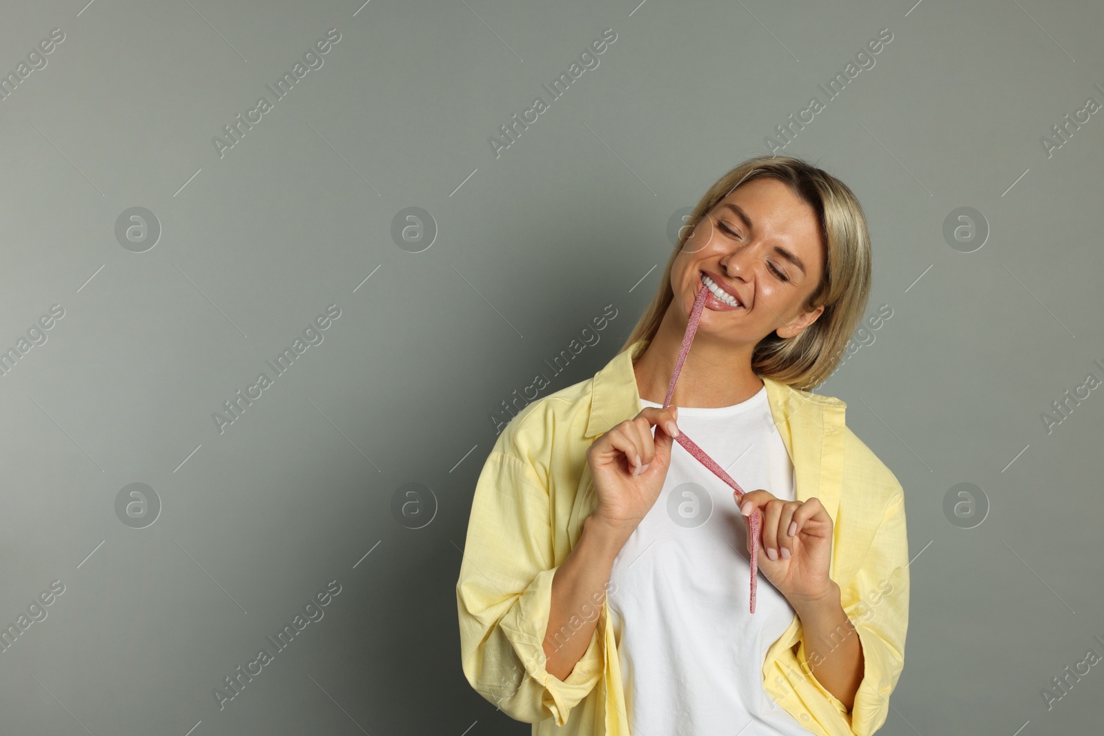 Photo of Young woman eating tasty gummy candy on grey background, space for text