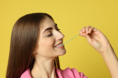 Photo of Young woman eating tasty gummy candy on yellow background, closeup