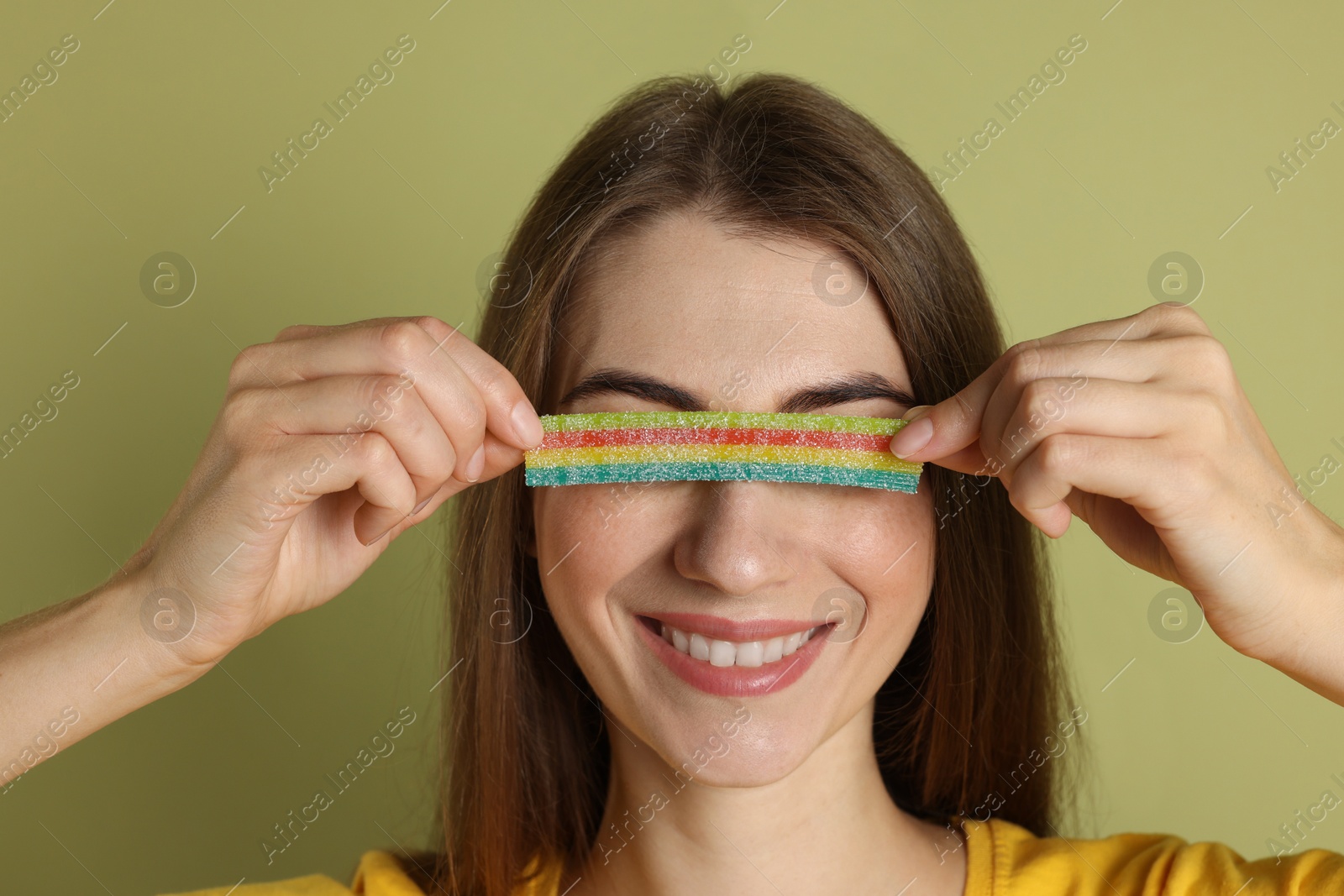 Photo of Young woman closing her eyes with tasty rainbow sour belt on olive background, closeup