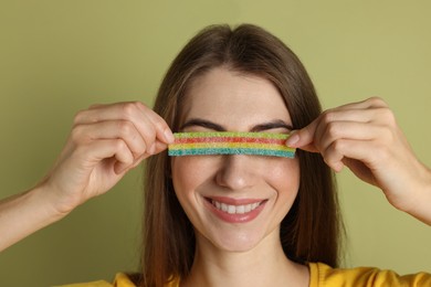 Photo of Young woman closing her eyes with tasty rainbow sour belt on olive background, closeup