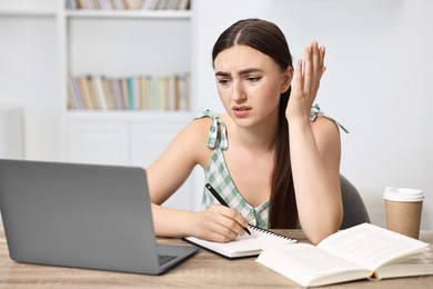 Photo of Tired student preparing for exam with laptop at table indoors