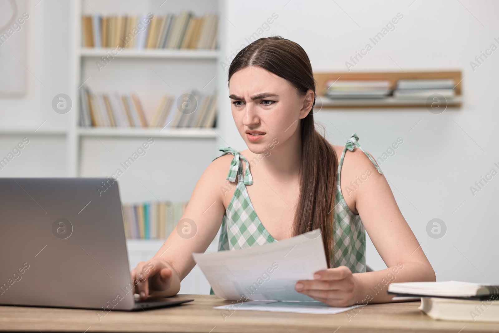 Photo of Tired student preparing for exam with laptop at table indoors