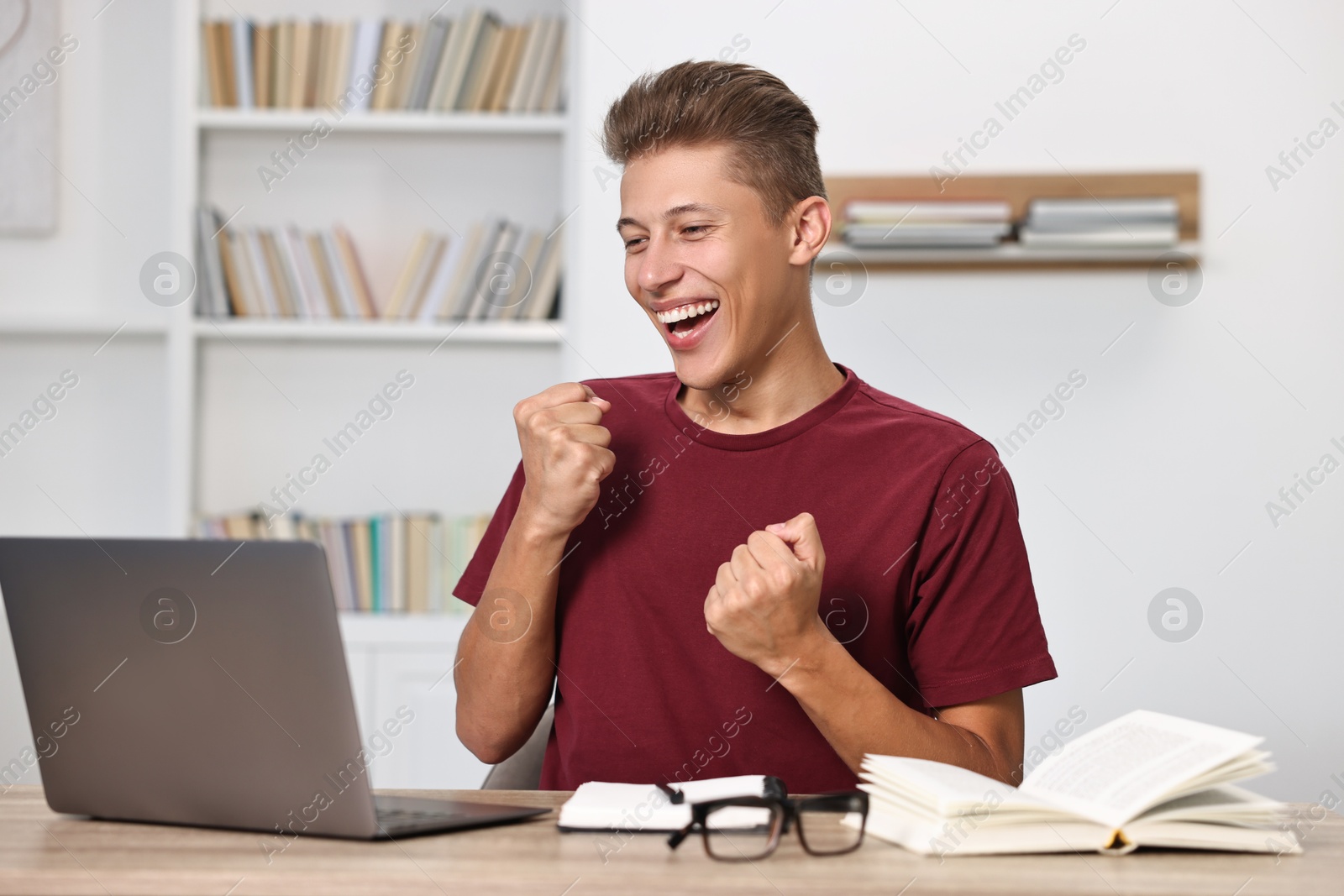 Photo of Student feeling happy about his good exam result at table with laptop indoors