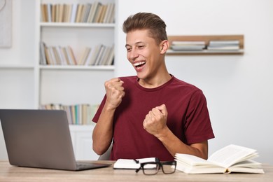 Student feeling happy about his good exam result at table with laptop indoors