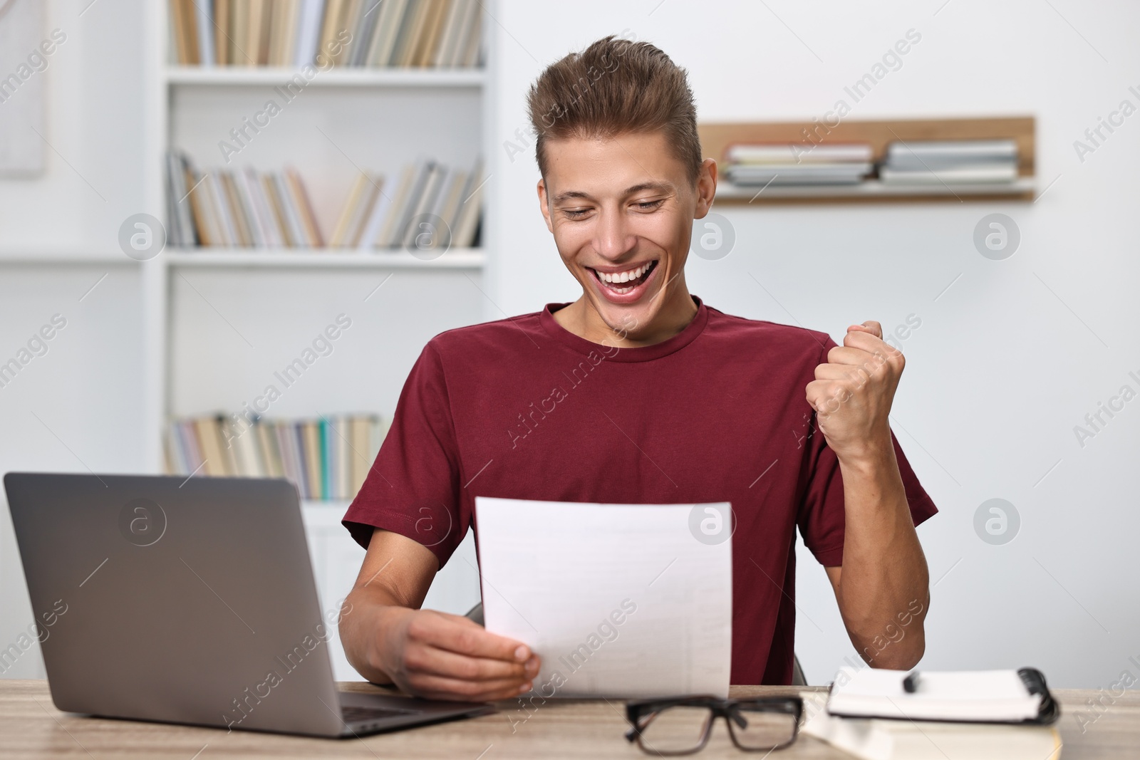 Photo of Happy student reading his good exam result at table indoors