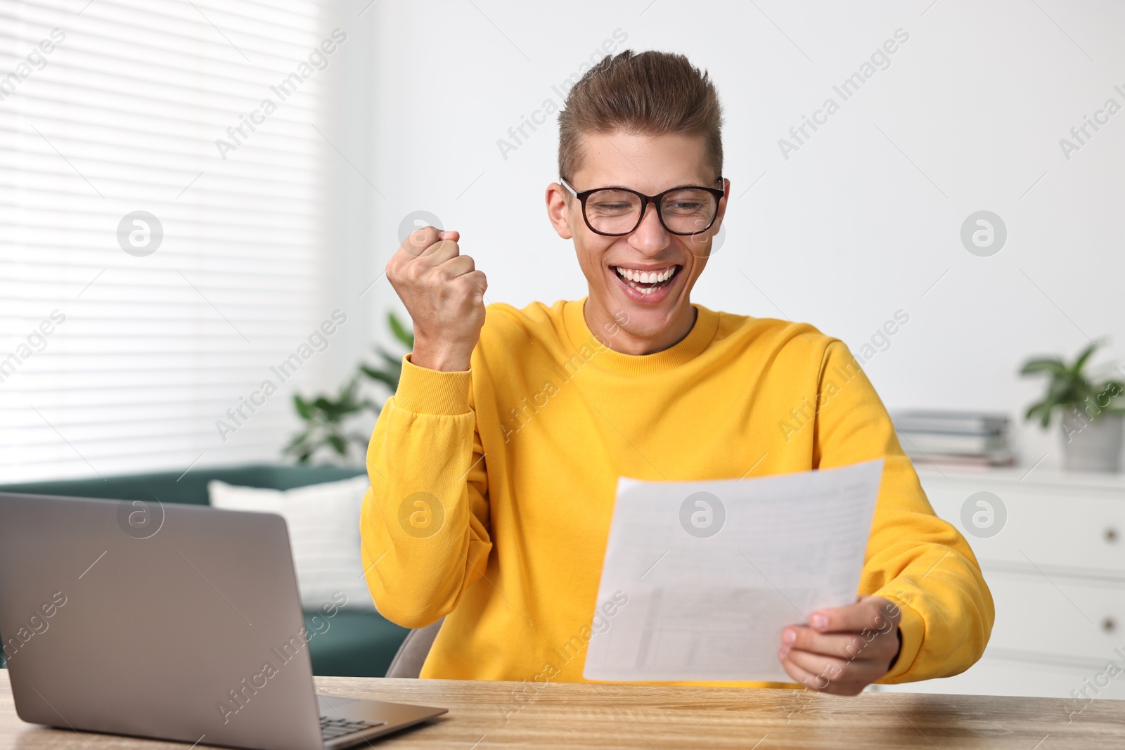 Photo of Happy student reading his good exam result at table indoors