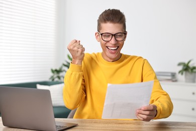 Happy student reading his good exam result at table indoors