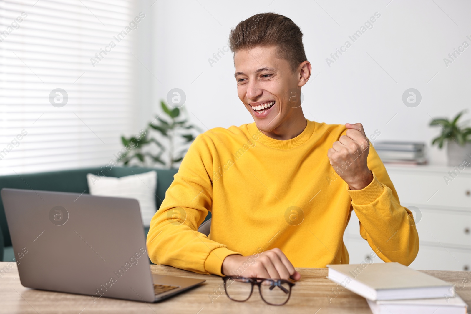 Photo of Student feeling happy about his good exam result at table with laptop indoors