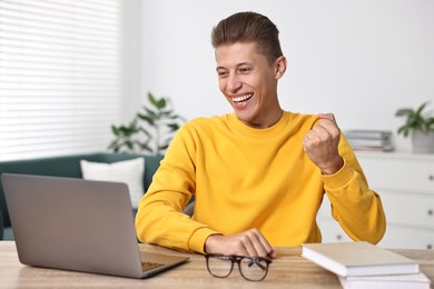 Photo of Student feeling happy about his good exam result at table with laptop indoors