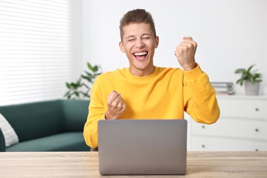 Photo of Student feeling happy about his good exam result at table with laptop indoors