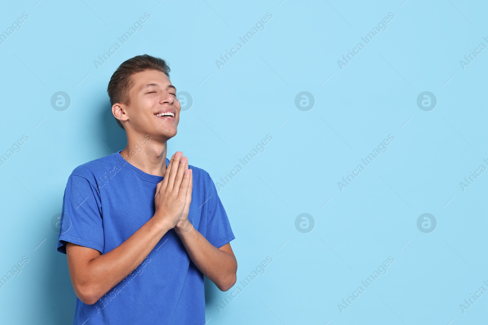 Photo of Happy student praying for good exam result on light blue background. Space for text