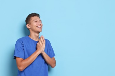 Photo of Happy student praying for good exam result on light blue background. Space for text