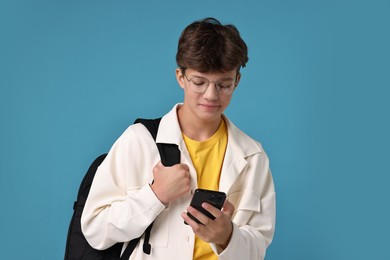 Photo of Teenage boy with smartphone and backpack on light blue background