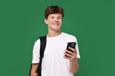 Photo of Teenage boy with smartphone and backpack on green background