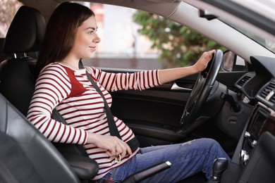 Photo of Pregnant woman fastening safety belt in car