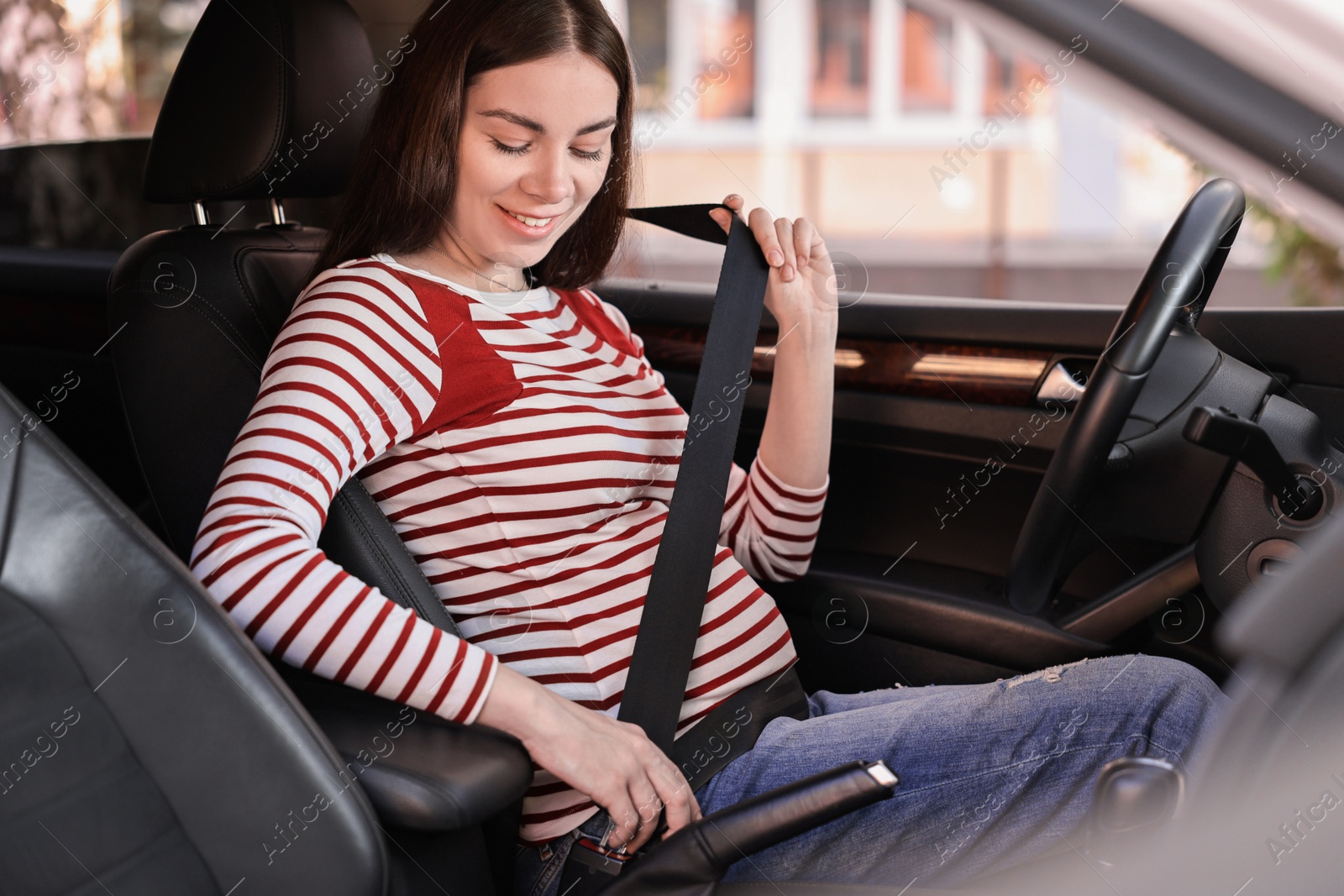 Photo of Smiling pregnant woman fastening safety belt in car