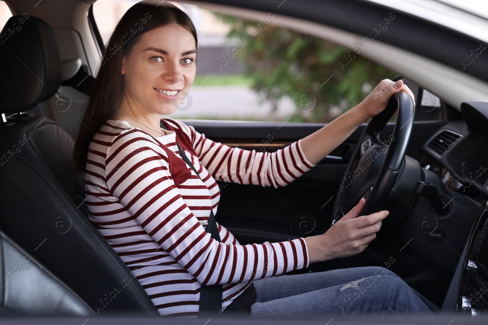 Photo of Smiling pregnant woman with safety belt driving car