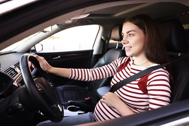 Photo of Smiling pregnant woman with safety belt driving car