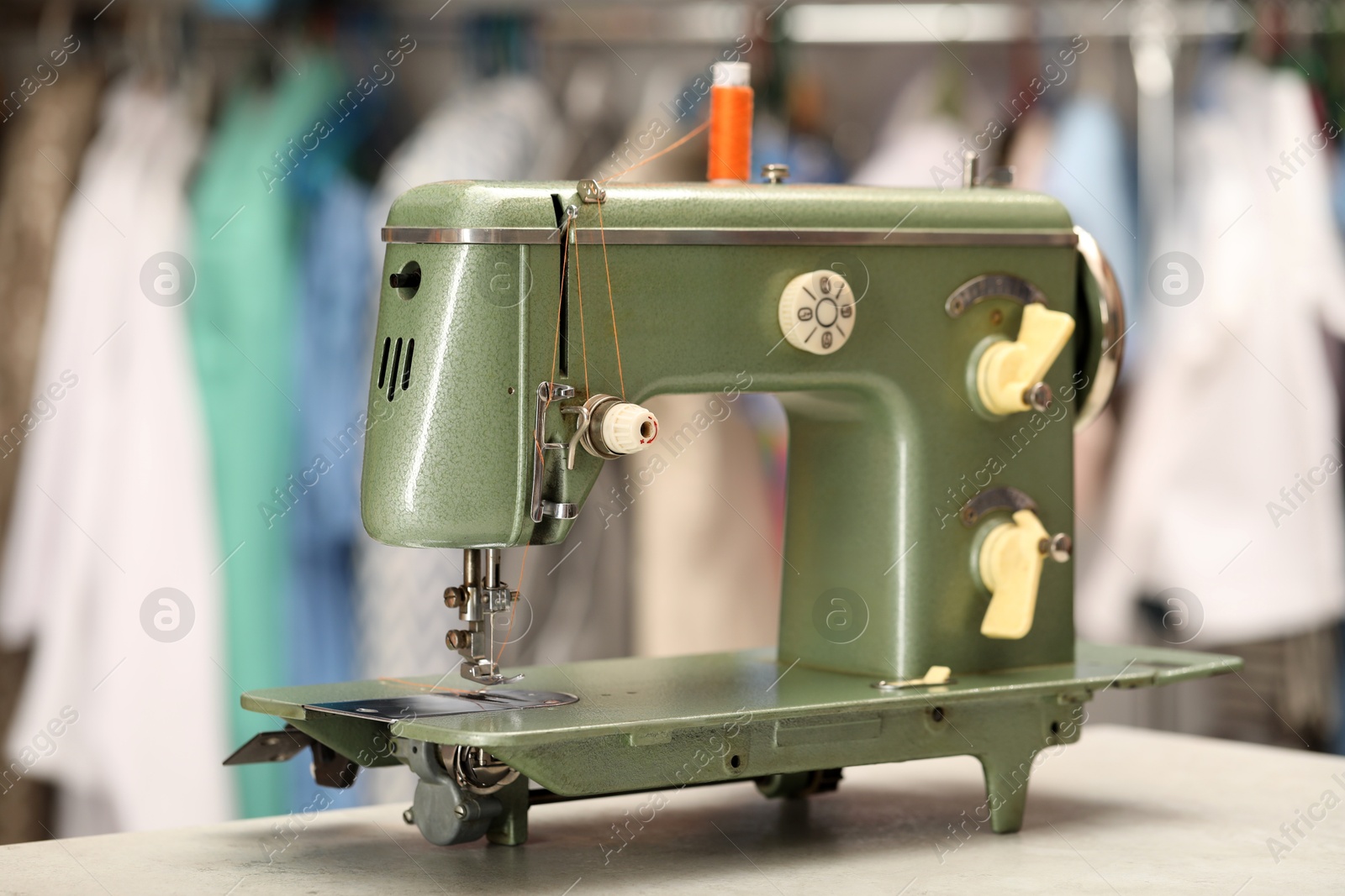 Photo of Vintage sewing machine with thread on white table in workshop, closeup