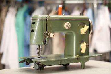 Photo of Vintage sewing machine with thread on white table in workshop, closeup