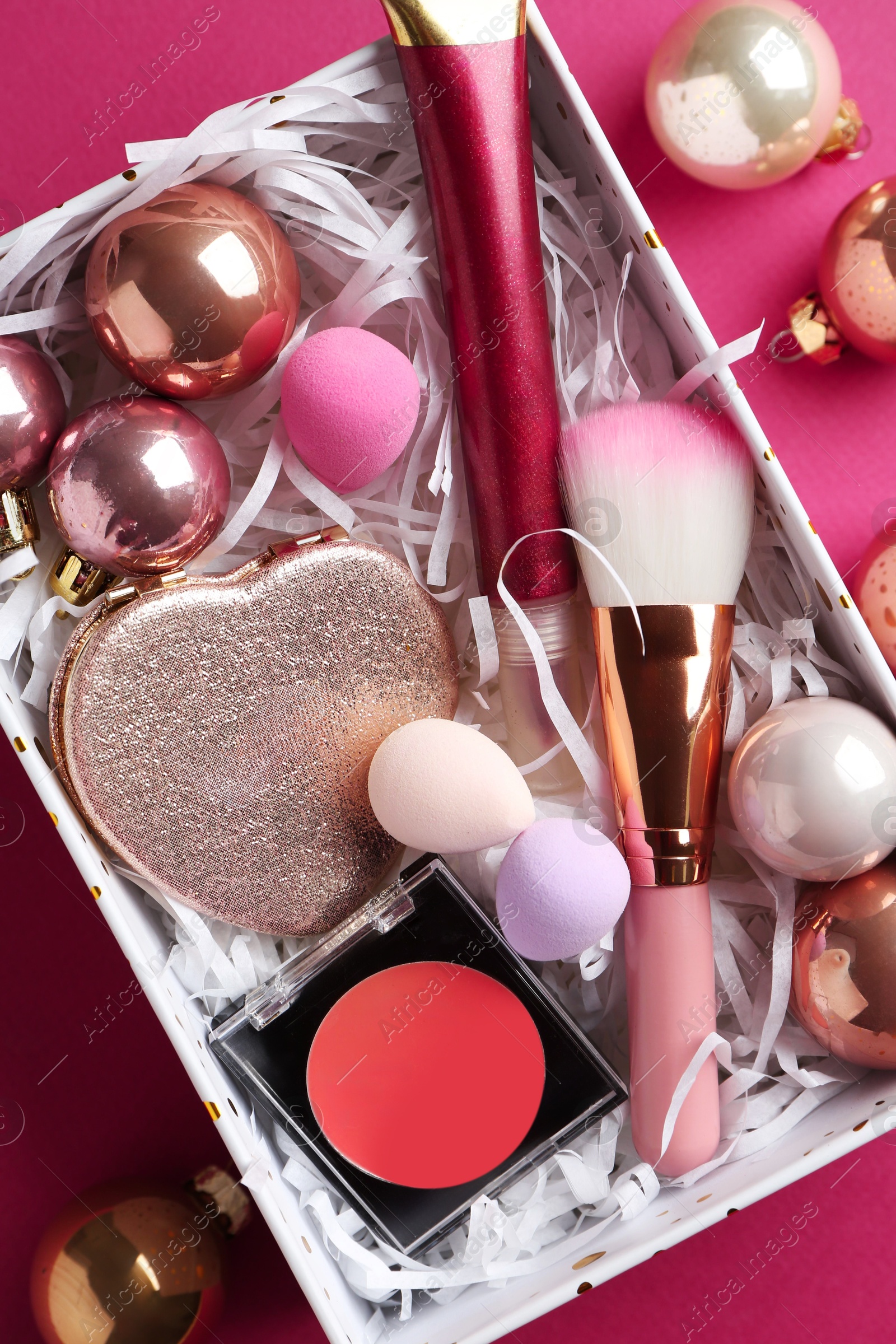 Photo of Christmas present. Decorative cosmetics in gift box and festive balls on dark pink background, top view