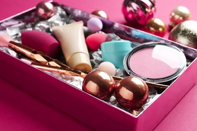 Photo of Christmas present. Decorative cosmetics in gift box and festive balls on dark pink background, closeup