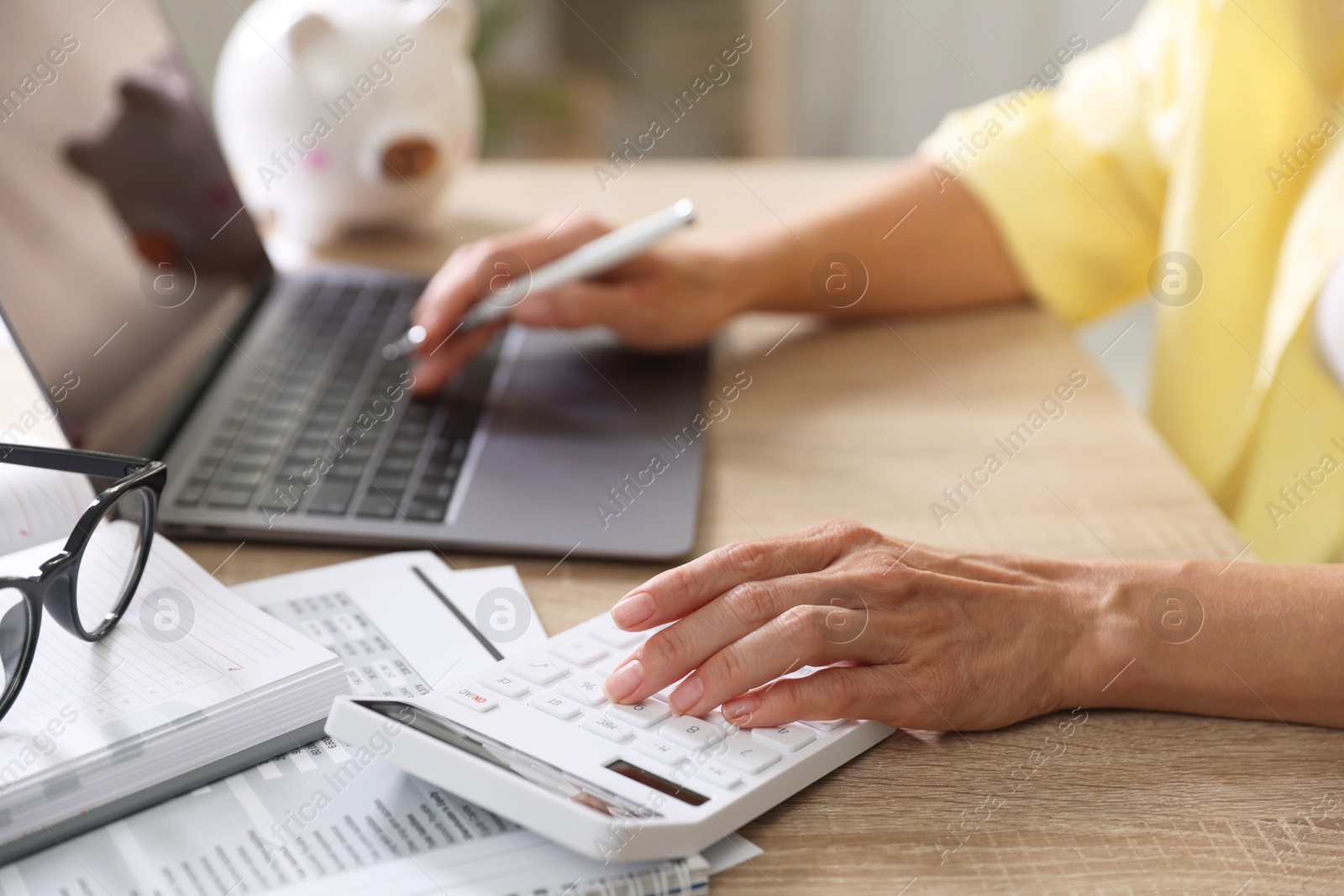 Photo of Budget planning. Woman working on laptop while using calculator at table indoors, closeup