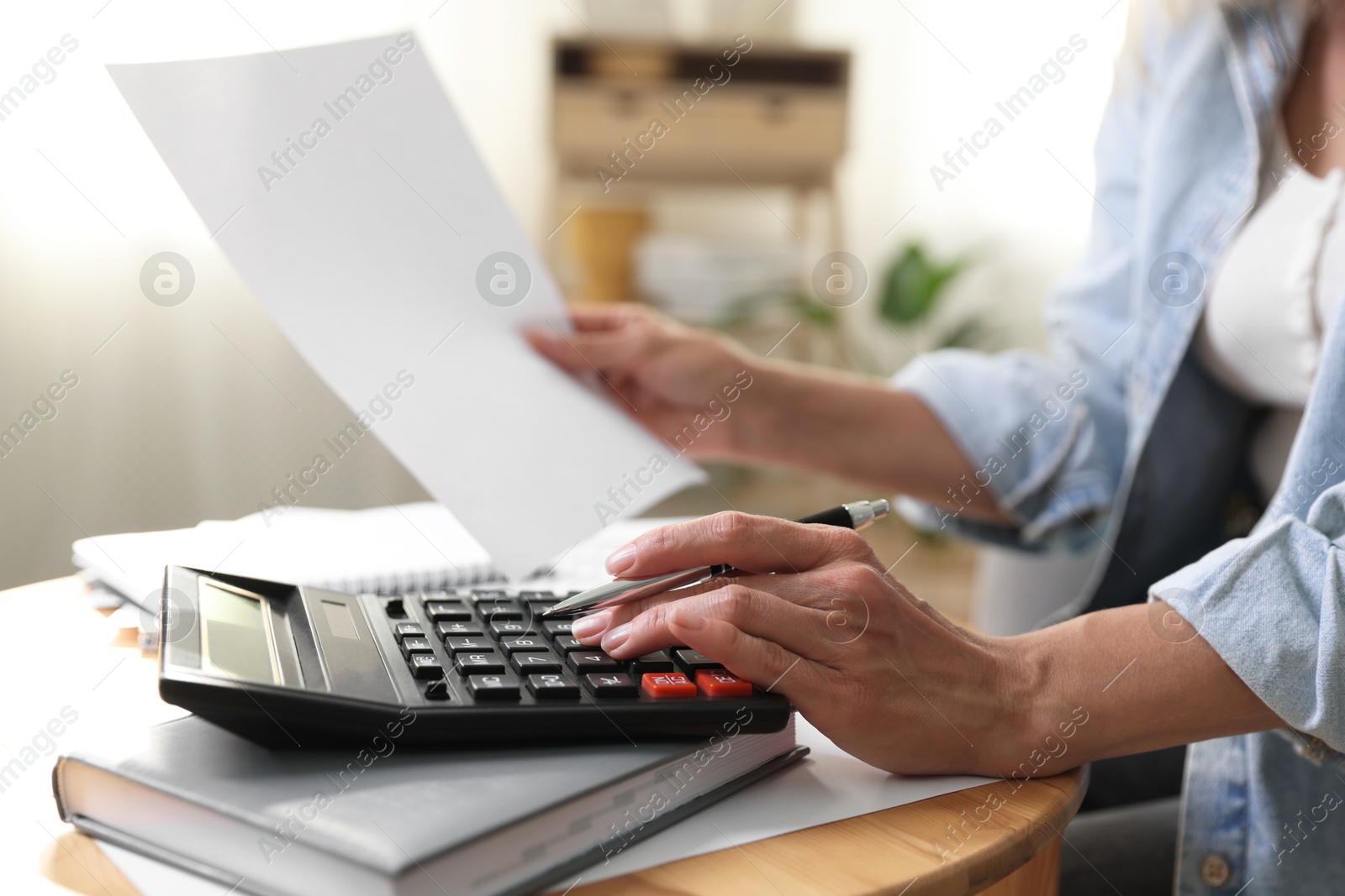 Photo of Budget planning. Woman using calculator while working with accounting document at table indoors, closeup