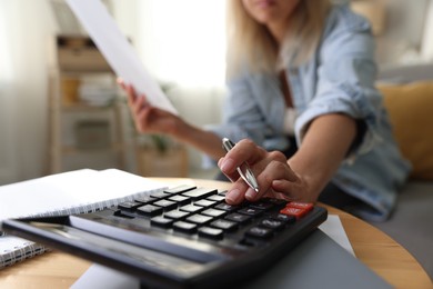 Photo of Budget planning. Woman using calculator while working with accounting document at table indoors, closeup