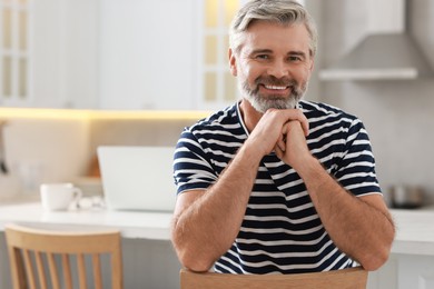 Photo of Happy middle aged man on chair in kitchen, space for text