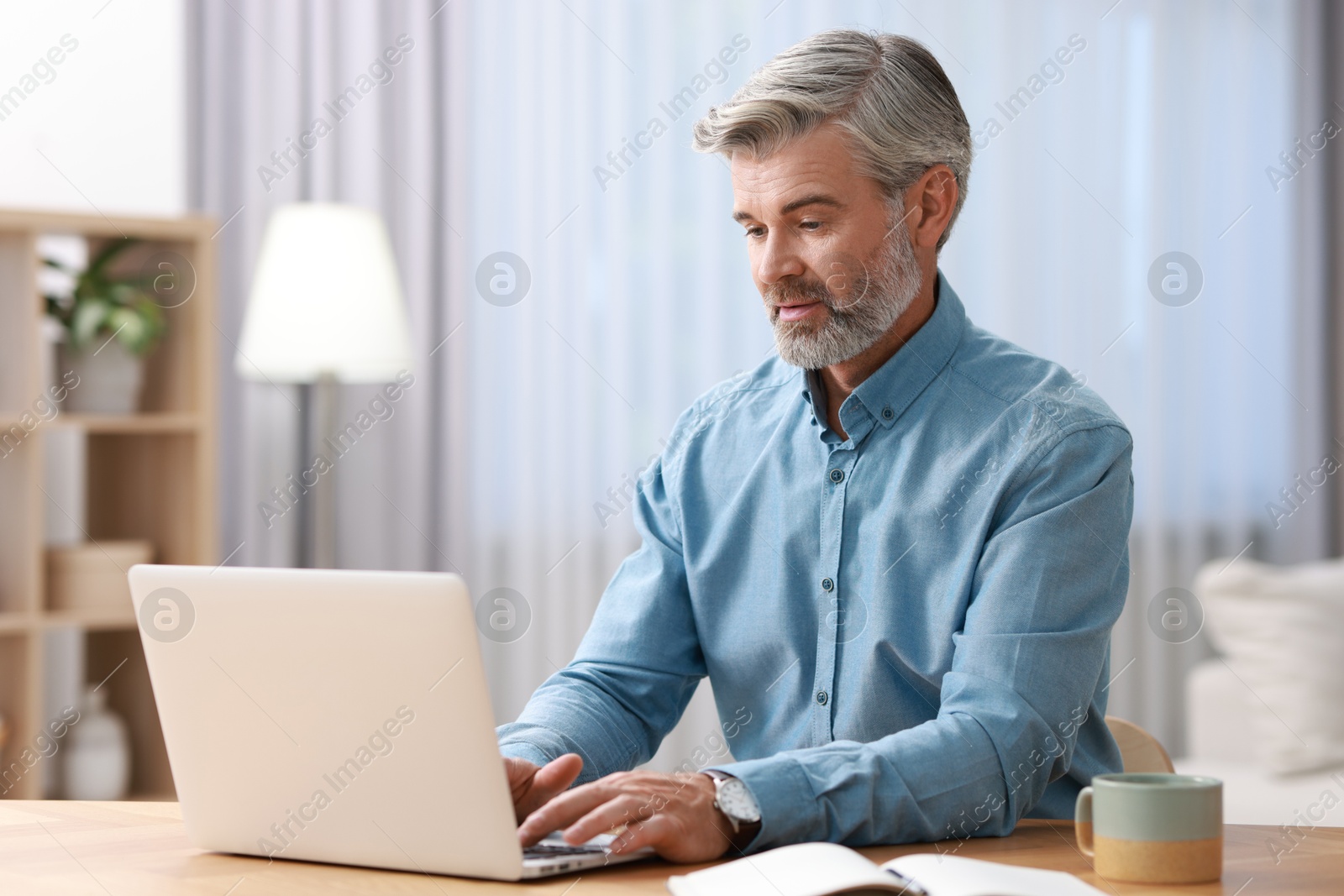 Photo of Middle aged man working with laptop at table indoors