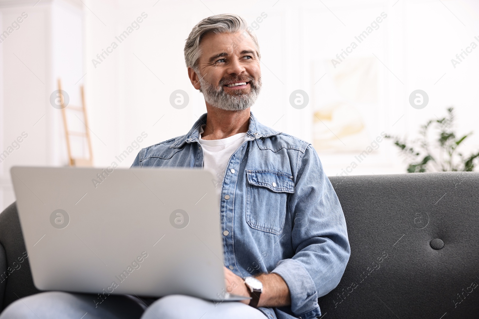 Photo of Happy middle aged man using laptop on sofa at home