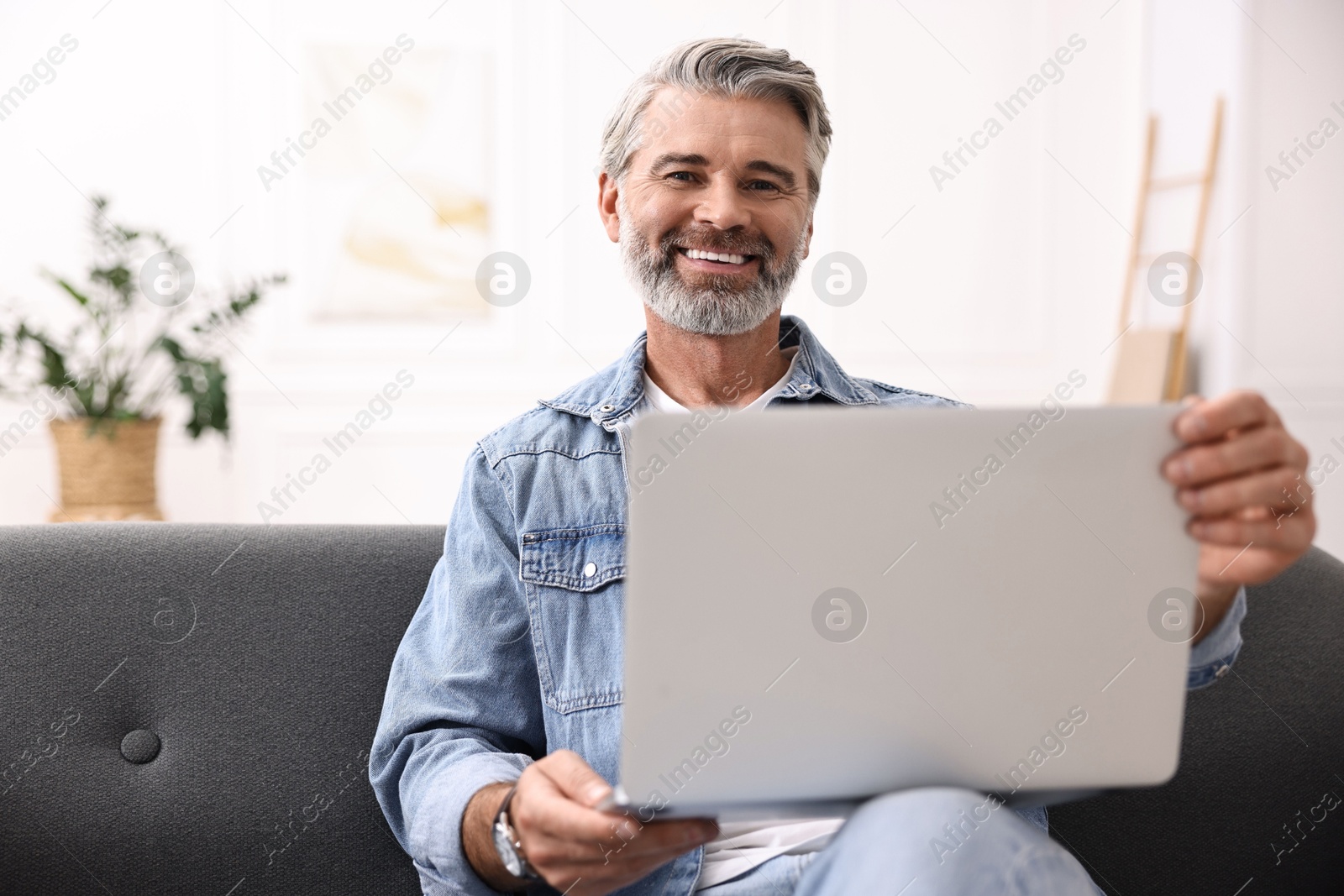 Photo of Happy middle aged man using laptop on sofa at home