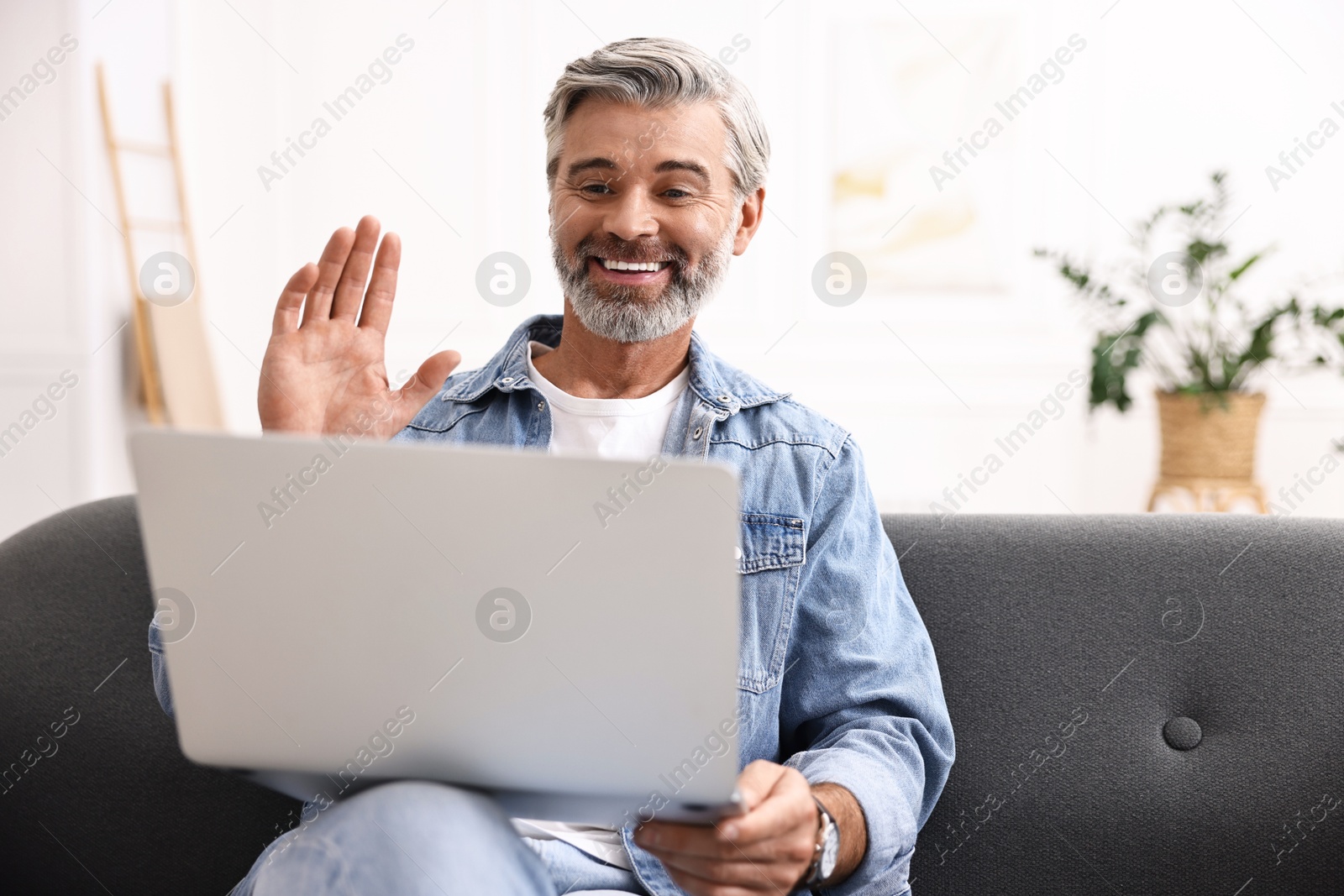 Photo of Happy middle aged man having video chat via laptop on sofa indoors