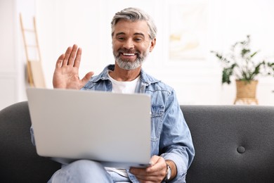 Photo of Happy middle aged man having video chat via laptop on sofa indoors