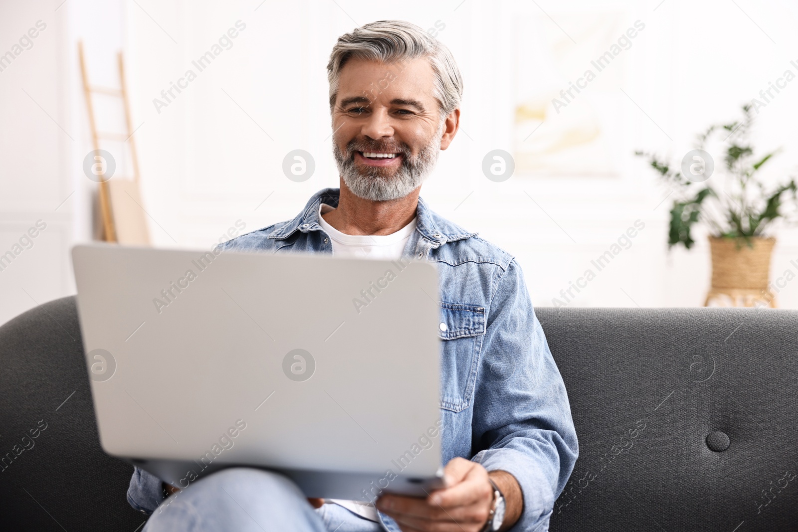 Photo of Happy middle aged man using laptop on sofa at home