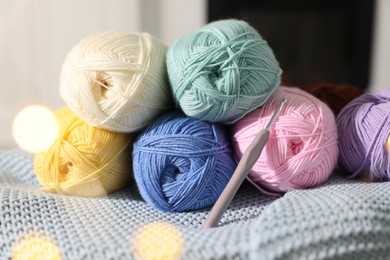 Photo of Many colorful yarns and crochet hook on blanket among blurred lights, closeup