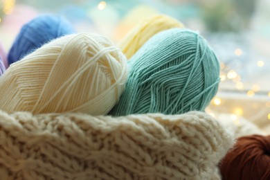 Photo of Many colorful yarns and sweater on blurred background, closeup