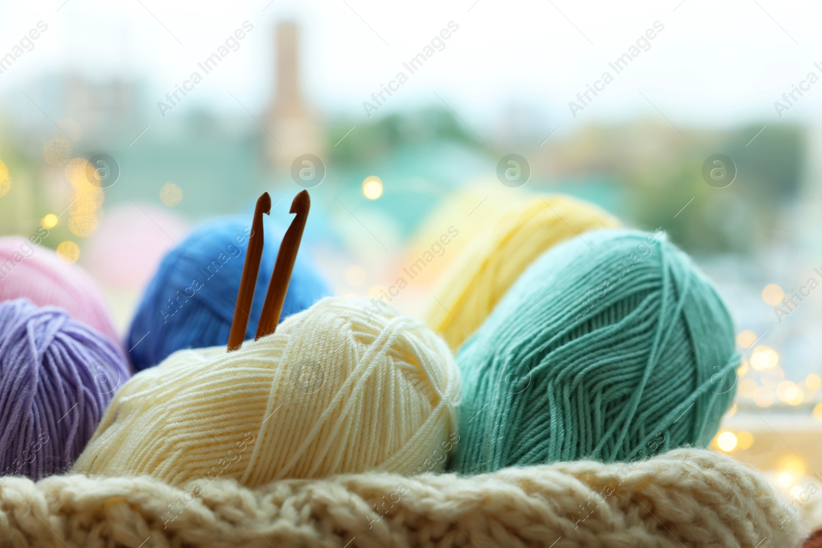 Photo of Many colorful yarns, crochet hooks and sweater on blurred background, closeup