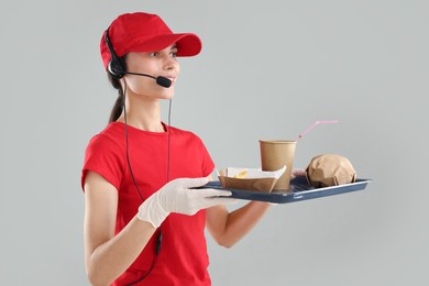 Fast-food worker holding tray with order on gray background,