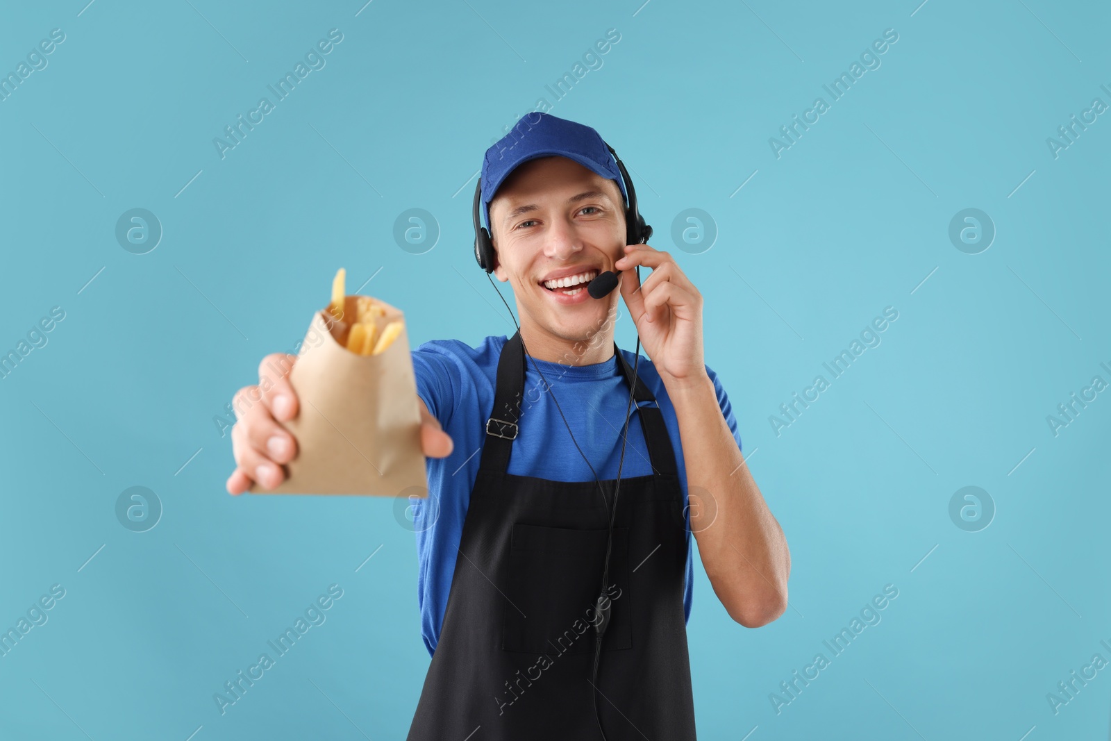 Photo of Fast-food worker with fries in paper bag on light blue background, selective focus