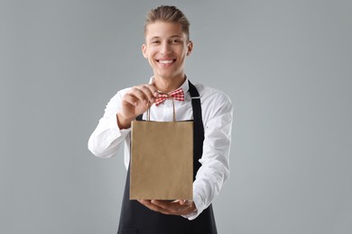 Fast-food worker with paper bag on gray background