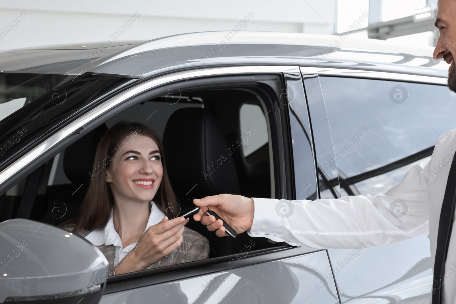 Photo of Woman giving key to man inside new car in salon