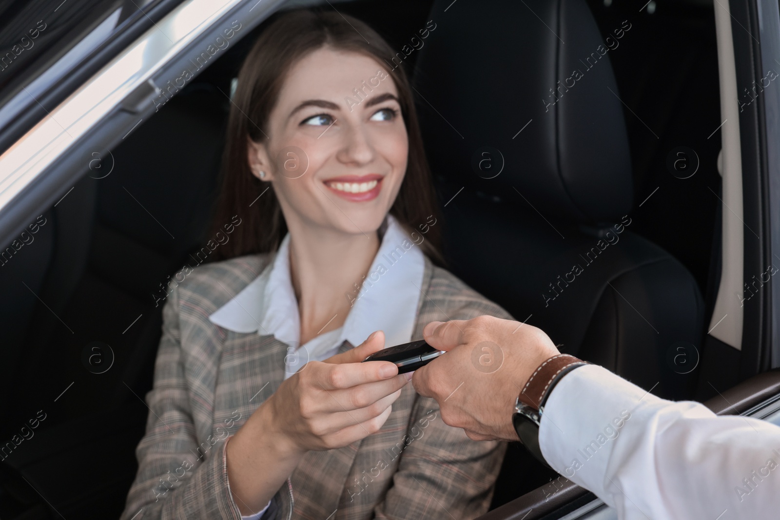 Photo of Salesman giving key to client inside new car in salon