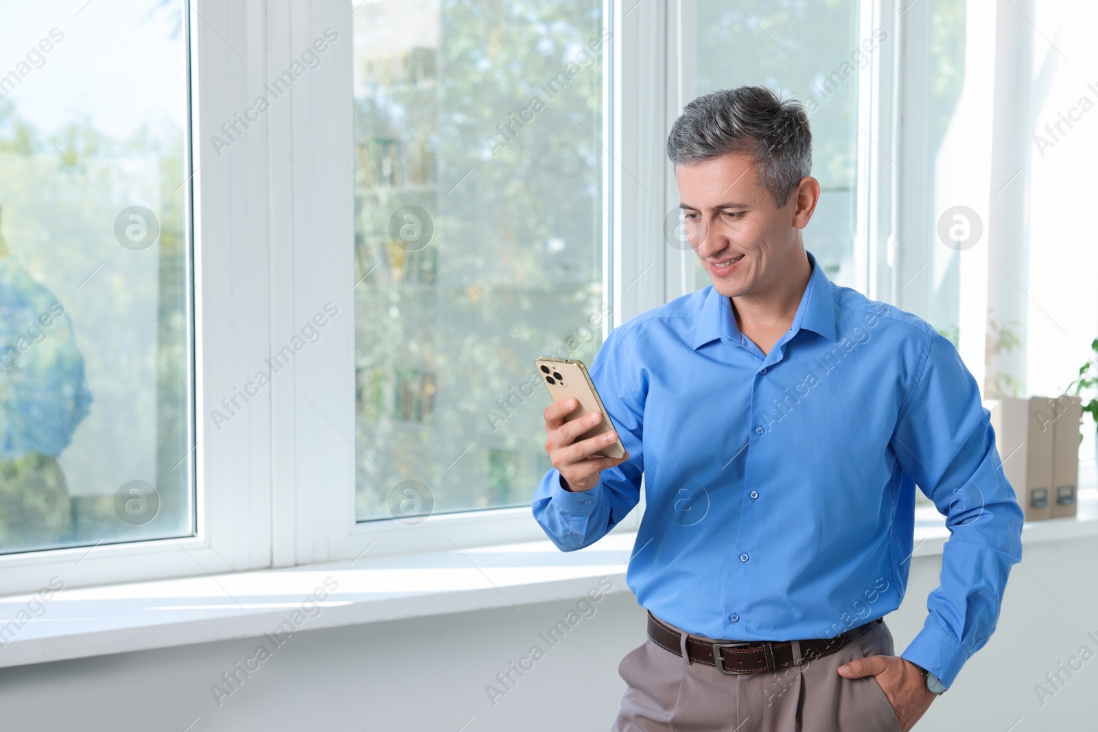 Photo of Smiling middle aged man using smartphone in office. Space for text