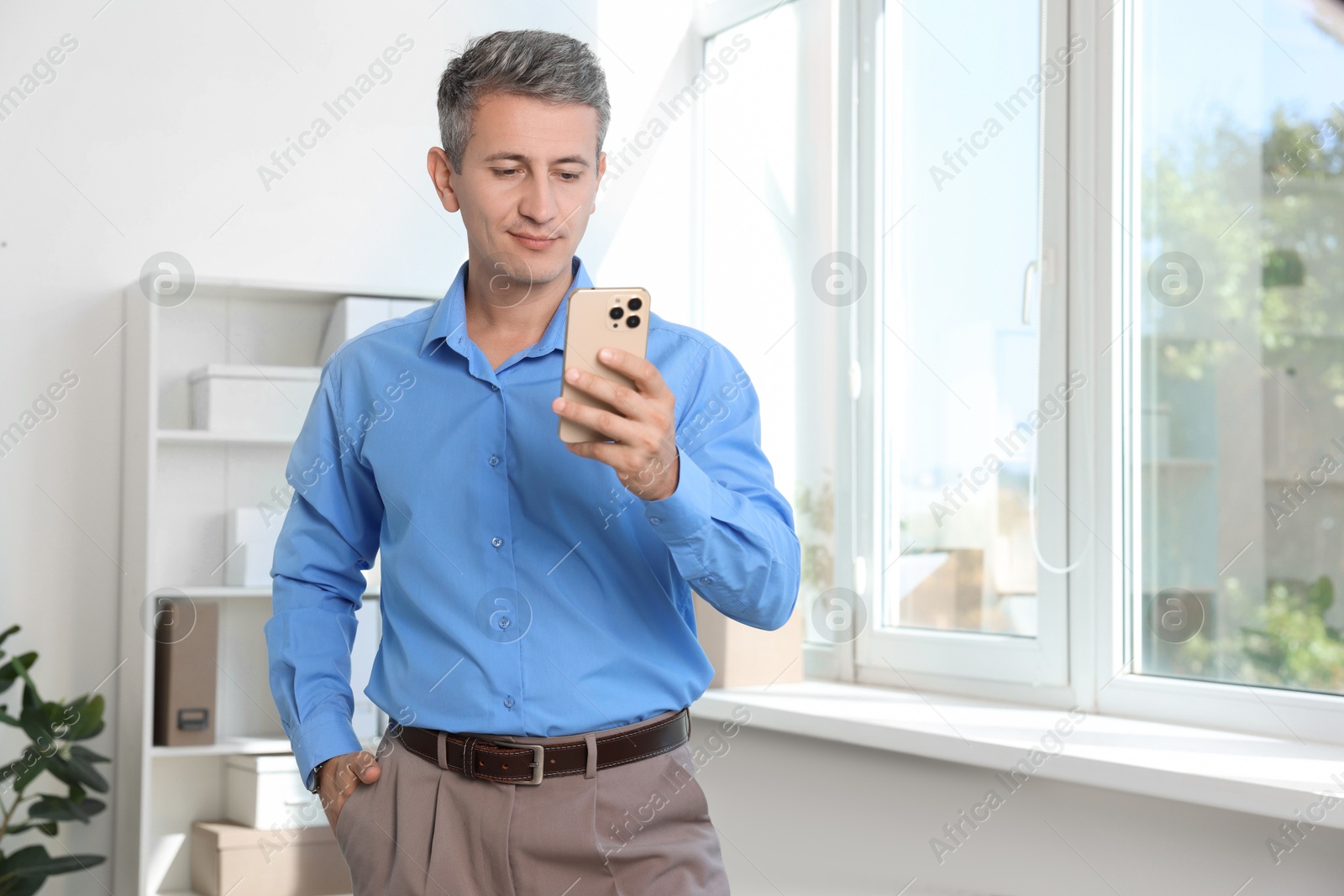 Photo of Middle aged man using smartphone in office. Space for text