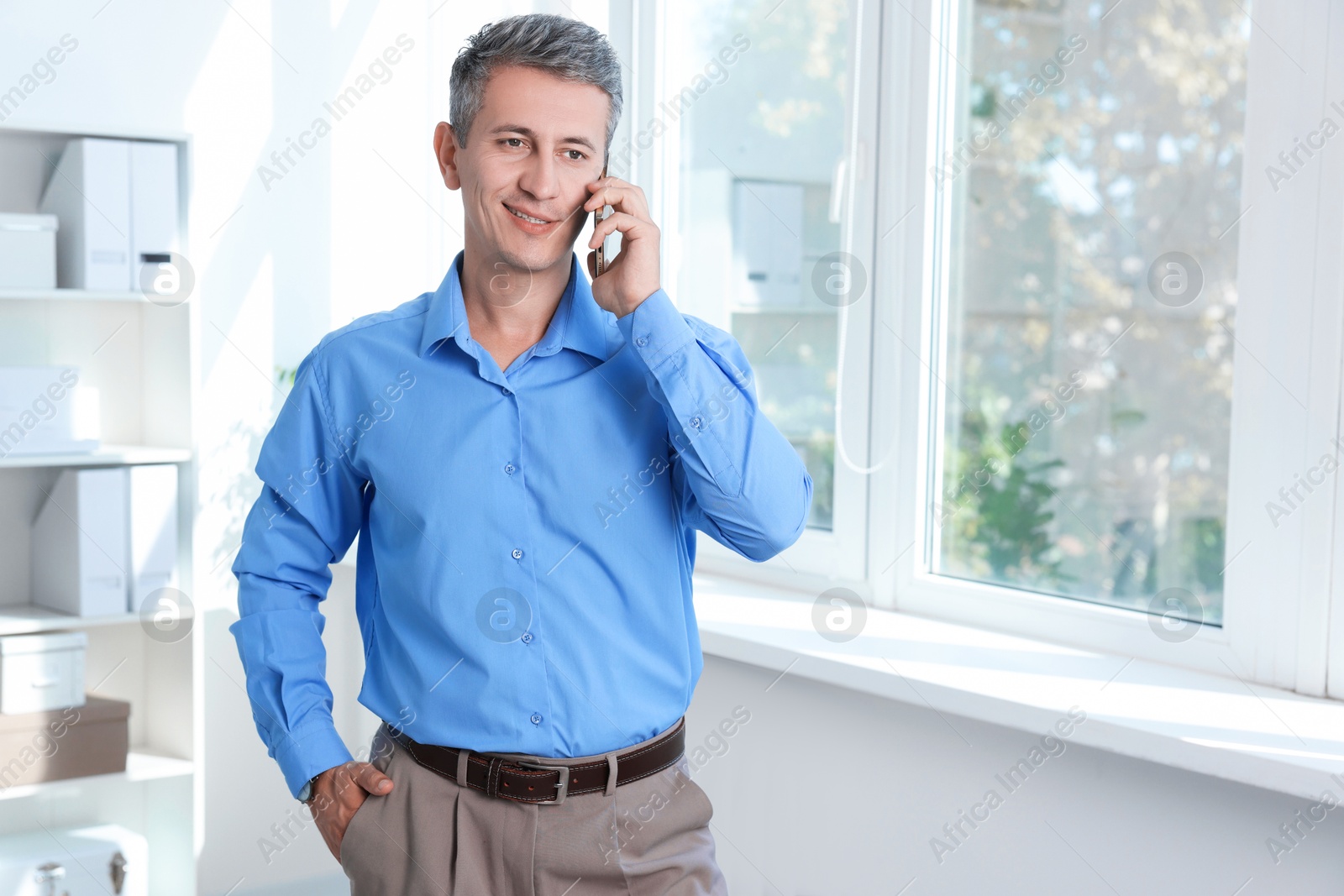 Photo of Smiling middle aged man talking by smartphone in office. Space for text