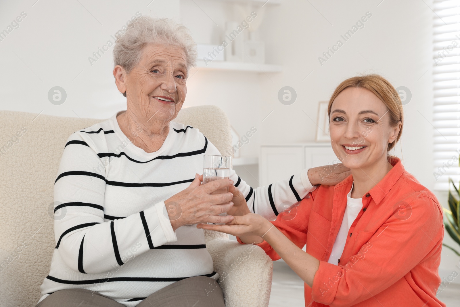 Photo of Caregiver giving glass of water to senior woman at home